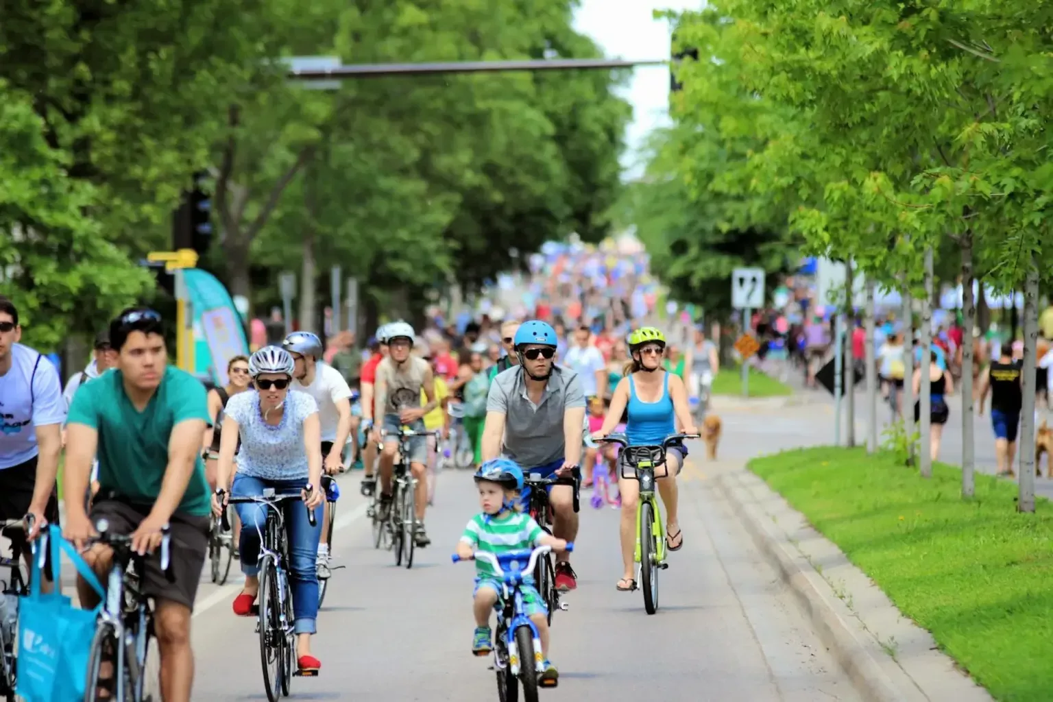 crowd of people biking down a street surrounded by trees