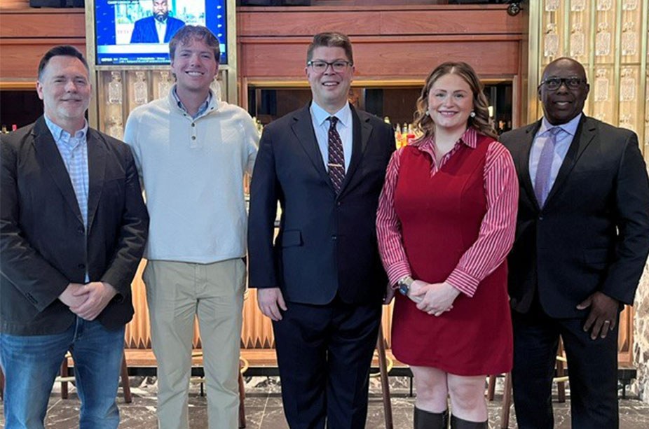 A group of five people stands in a row, smiling in the Stock & Bond Restaurant