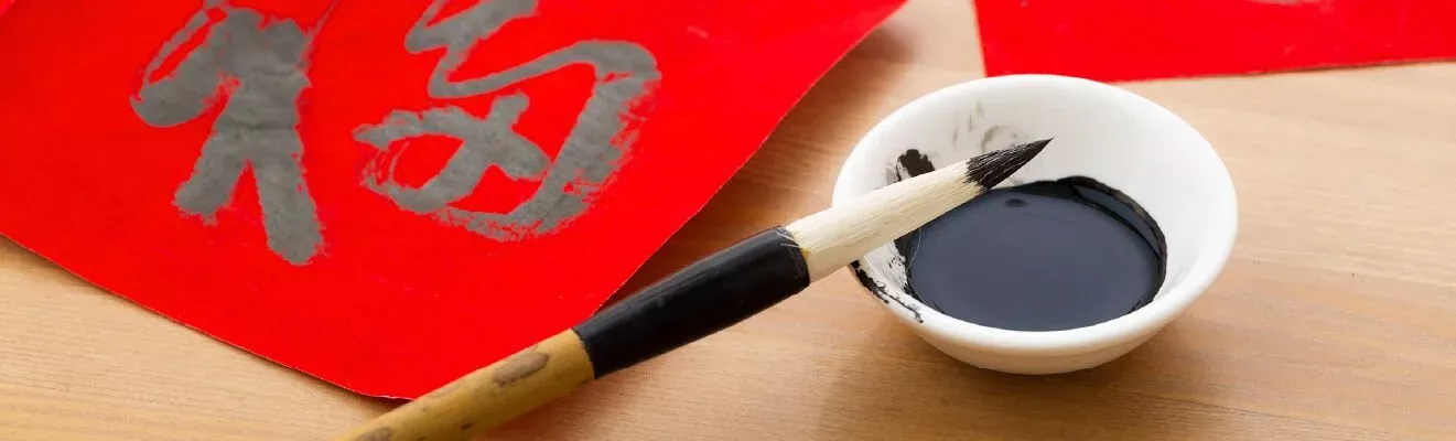 A Chinese calligraphy brush rests upon the lip of a shallow ceramic filled with calligraphy ink.