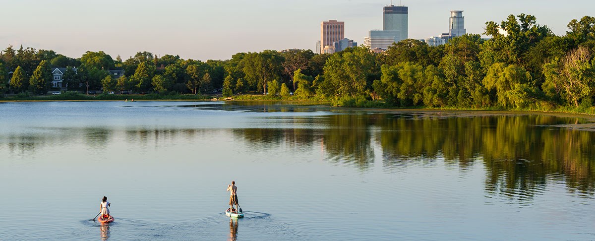 two people paddleboarding on lake with minneapolis skyline in the backaground